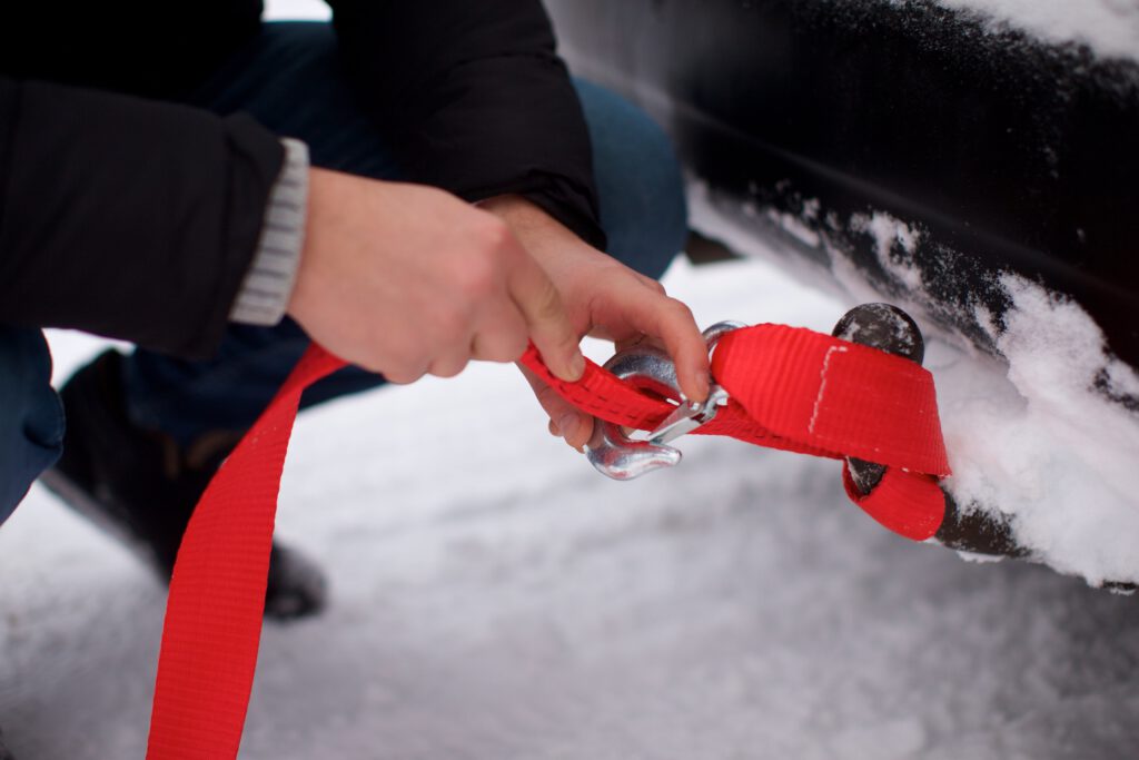 Eine Person befestigt ein Abschleppseil an der Fahrzeuganhängevorrichtung beim Wintercamping im Schnee.