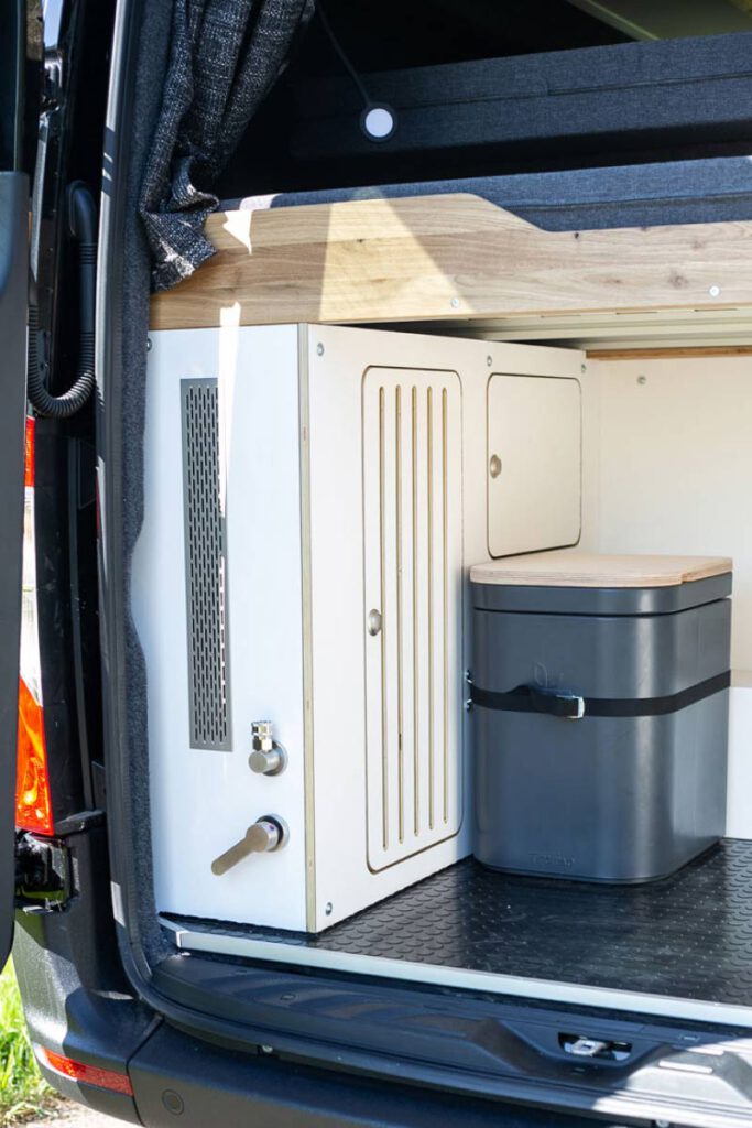 Ein Vanside Campervan Ausbau mit Blick ins Heck, mit dem Wassersystem und das Sanitärsystem hinter einer Verkleidung.