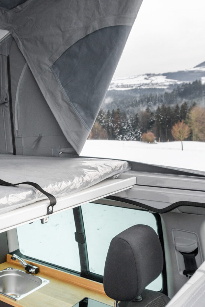 Das innere eines Campervans bei geöffnetem Zeltdach, das zum Lüften beim Wintercamping für frische Luft sorgt.